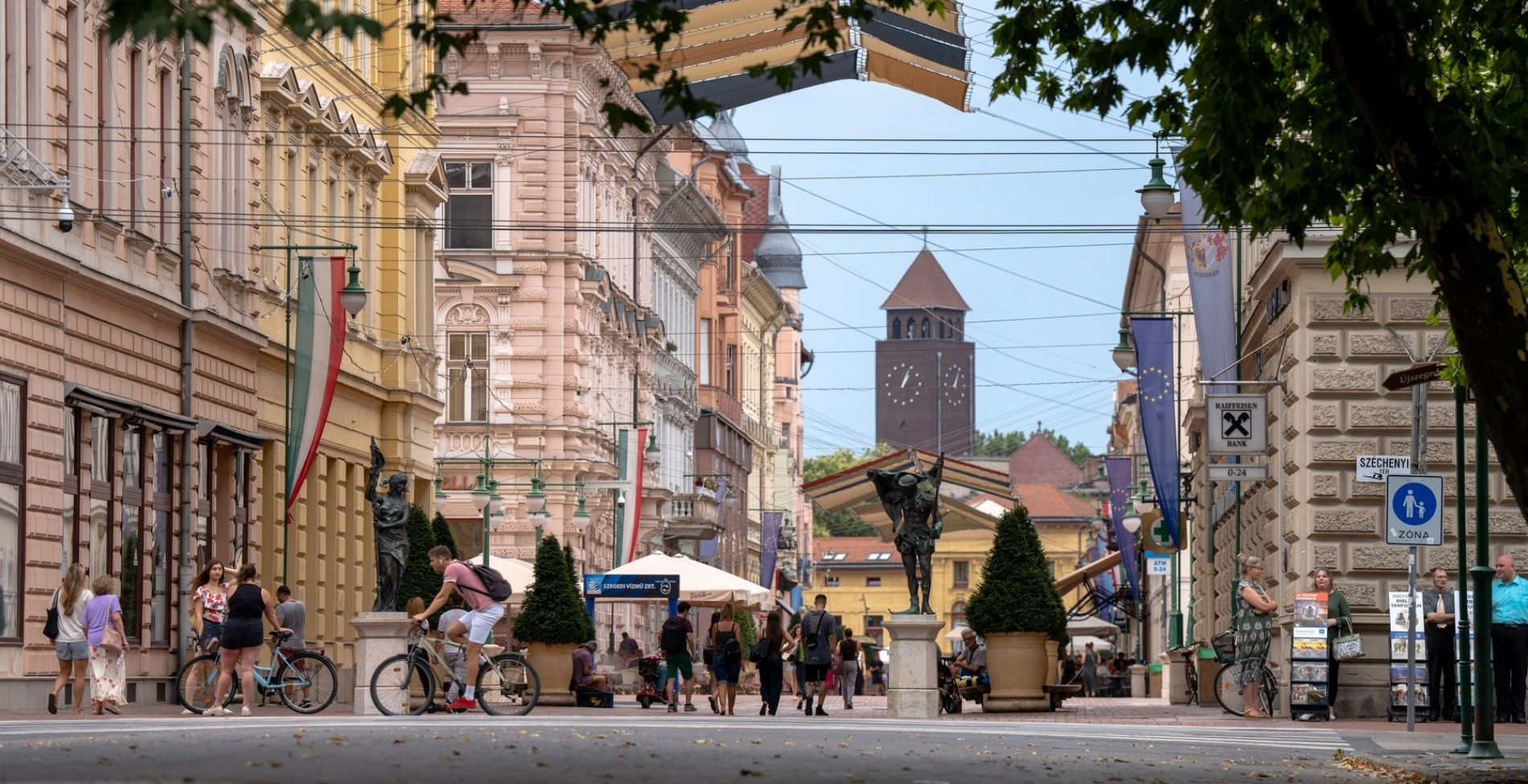 zeged, a patinás magyar város sétálóutcája, ahol a háttérben látható szobrok a digitális technológia és a mesterséges intelligencia révén kelnek életre a videóban.