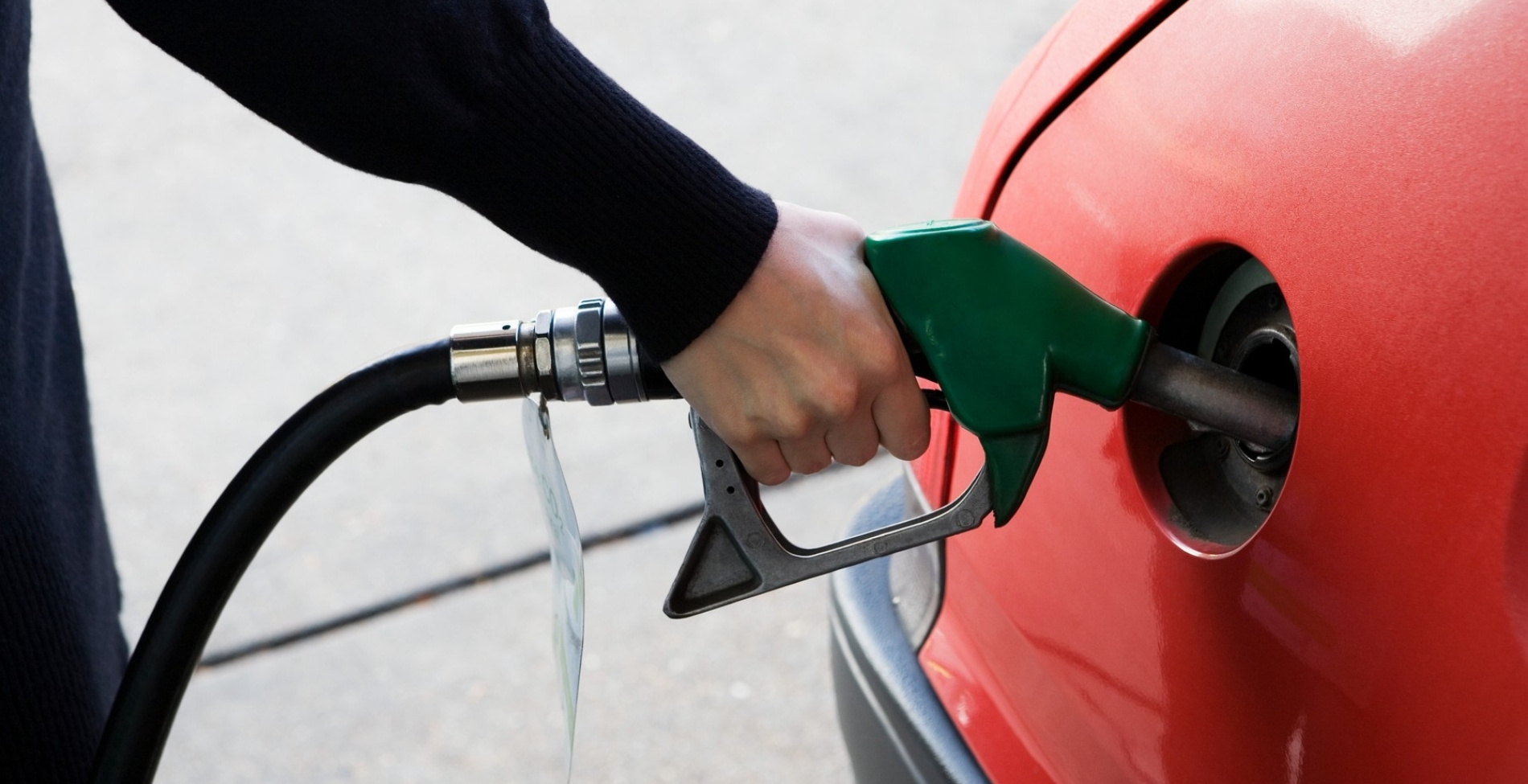 Közeli felvétel egy tankolásról, ahol egy zöld töltőpisztolyt helyeznek egy piros autó üzemanyagtartályába, szemléltetve a mol benzinkút hálózatában tapasztalható aktuális üzemanyagárak és a magyar kormány intézkedéseinek közvetlen hatását a fogyasztókra.